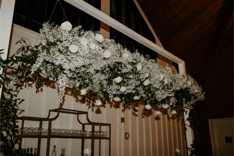 Hanging garden above bar at wedding of varying white florals. 