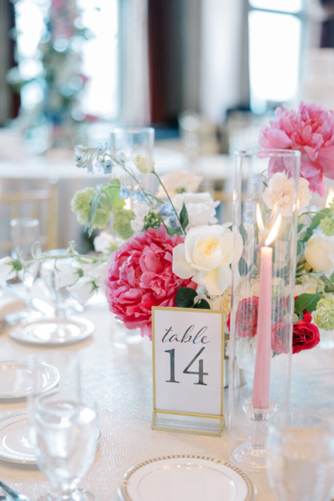 Wedding decor centerpiece of table number, pink candles, and bright pink and white seasonal floral centerpiece.