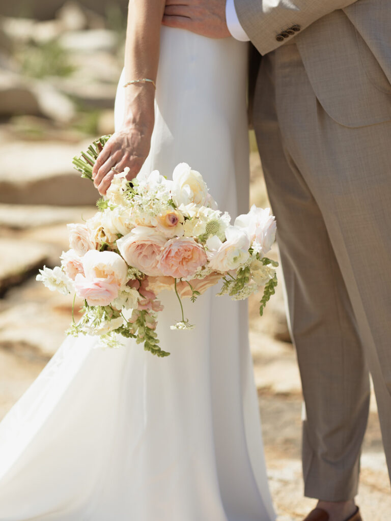 Bride holding bouquet of seasonal florals featuring light pink hues. 