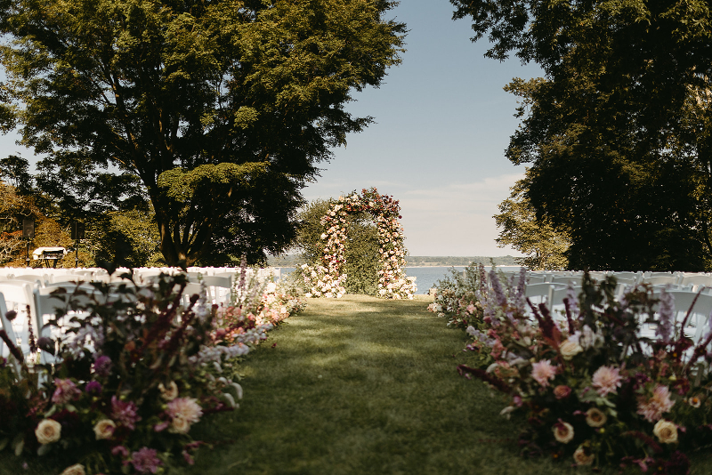 View from end of wedding aisle looking at aisle arrangements and floral wedding arch using bright, local, and seasonal flowers. 