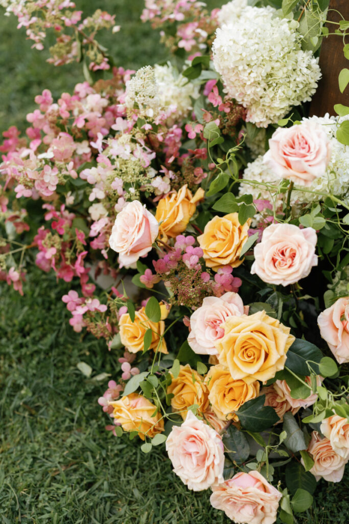 Close up of summer flower arrangement sitting at the base of arch. 