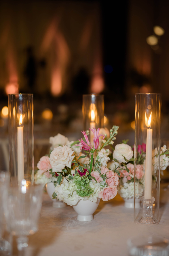 Delicate bud vases with blush, white, and green blooms paired with glowing taper candles in glass hurricanes