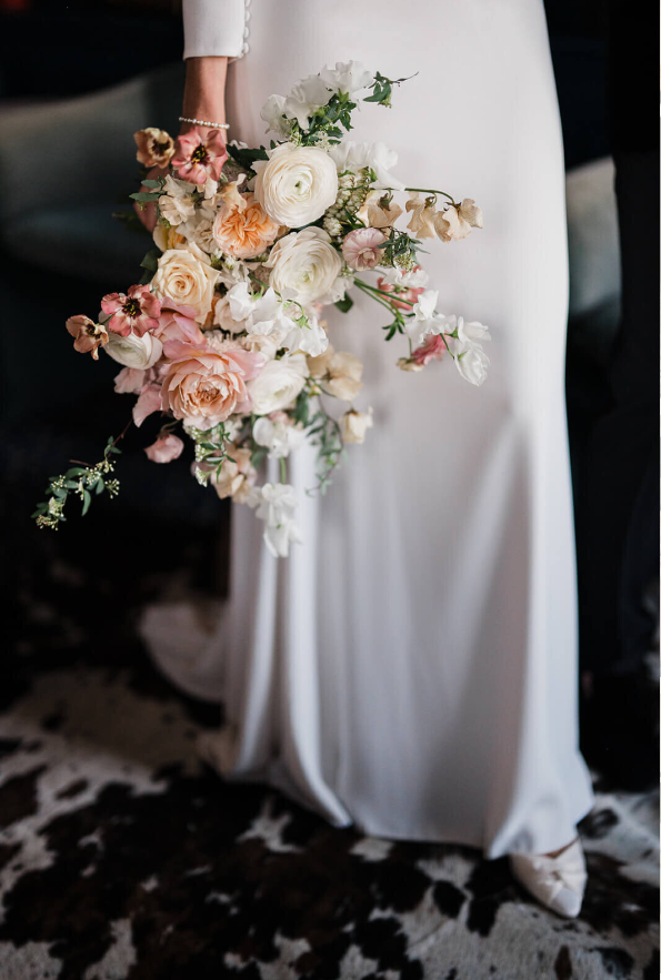 bride holding bouquet of blush and cream garden roses, ranunculus, sweet peas, and delicate greenery for an airy, elegant look.