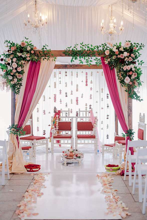 A vibrant mandap adorned with pink drapes, greenery, and cascading florals | wedding floral design budget