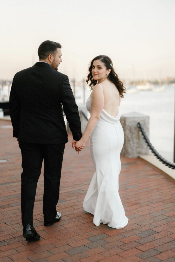 bride looking back as her and her husband walk along the harbor at the Boston Harbor Hotel 